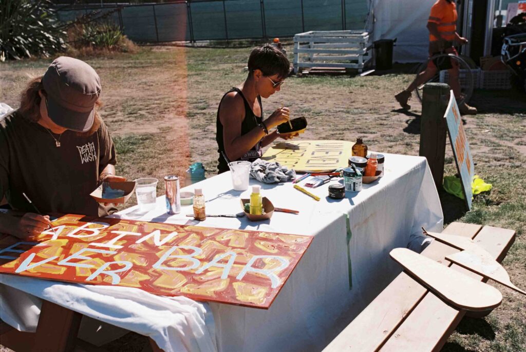 Two people sitting at bench, hand painting signs pre festival at TwoMinds 2026