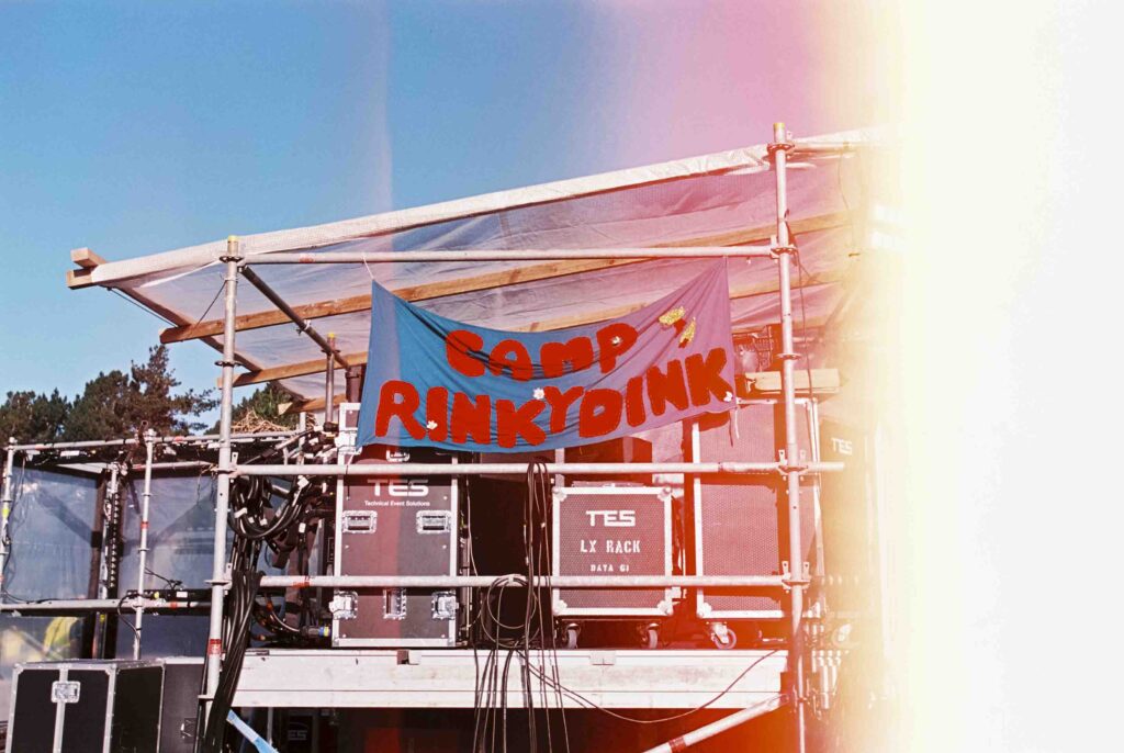 Film photo, backstage at TwoMinds 2026. Flag hanging from stage framing with words ‘camp Rinkydink’ on it